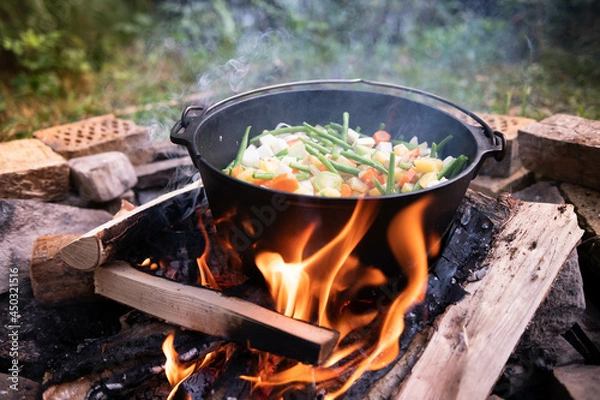 Fototapeta Dutch oven cooking on a campfire with open lid and stew