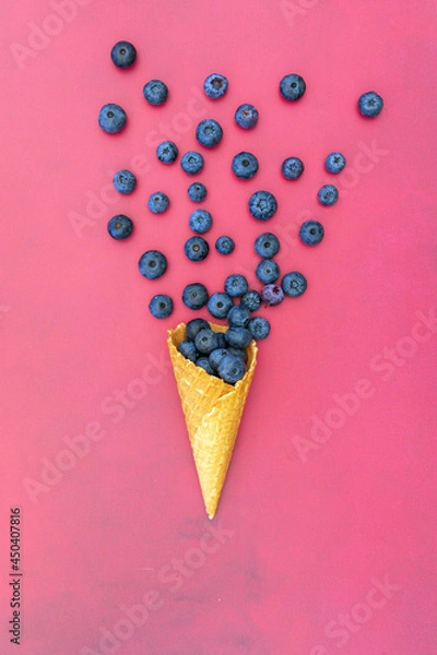 Obraz A portrait orientation shot from above flat lay shot of a single waffle ice cream cone overflowing with fresh blueberries shot on a contrasting red background with space for text
