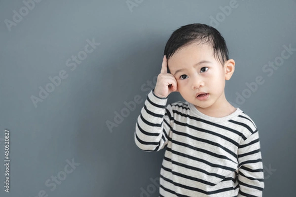 Fototapeta Portrait of thinking Asian baby boy with a grey isolated background.