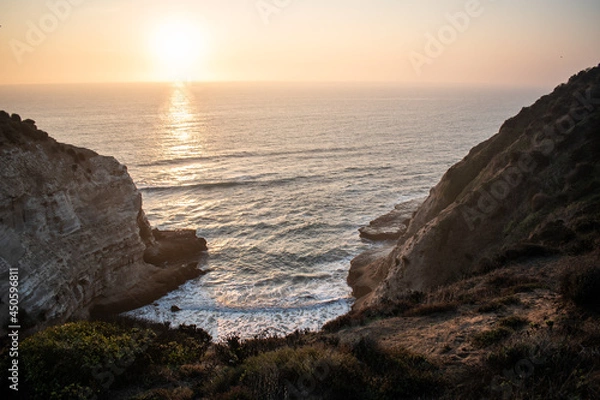 Fototapeta The sea between big cliffs on a beautiful sunset