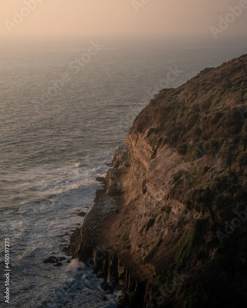 Fototapeta The sea in front of a big cliff on a beautiful sunset with zoom