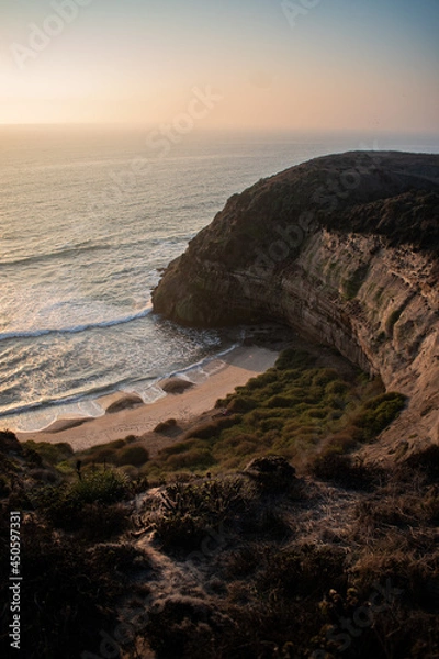 Fototapeta A beautiful beach between cliffs, with green shrubbery, at sunset