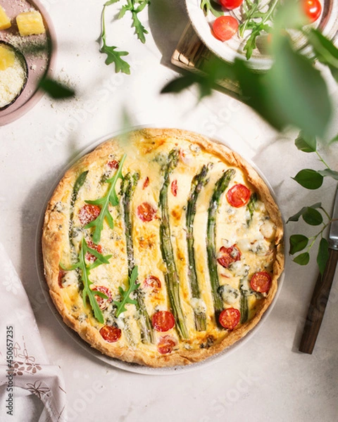 Obraz French cuisine. Quiche with asparagus, cherry tomatoes, and cheese. Summer food. Pie with cheese with blue mold and parmesan. Summer lunch on a light background. Pie made of fresh vegetables, arugula.