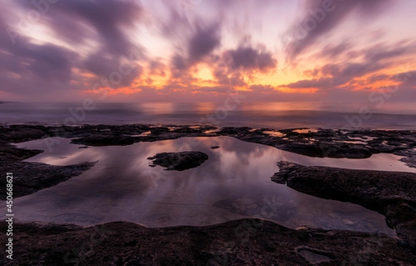 Obraz amazing scenic view at a sea shore from a coast after dramatic colorful sunset with flying blured clouds and reflection on water surface , beautiful ocean landscape