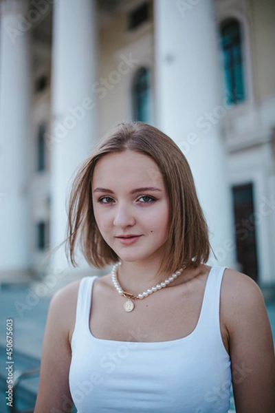 Obraz a beautiful girl in a skirt and top walks near the theater, looks into the frame, portrait, city girl