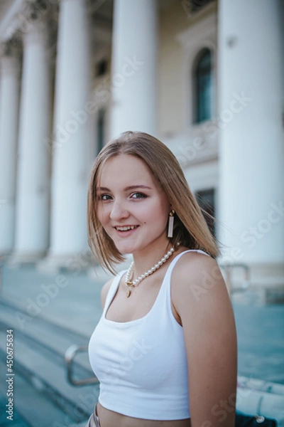 Obraz a beautiful girl in a skirt and top walks near the theater, looks into the frame, portrait, city girl