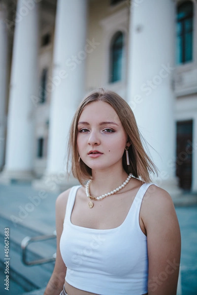 Obraz a beautiful girl in a skirt and top walks near the theater, looks into the frame, portrait, city girl