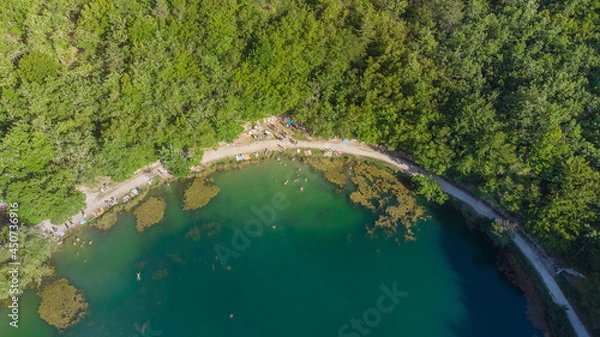 Fototapeta Small round lake full of swimmers sorrounded by trees during a sunny summer day aerial view