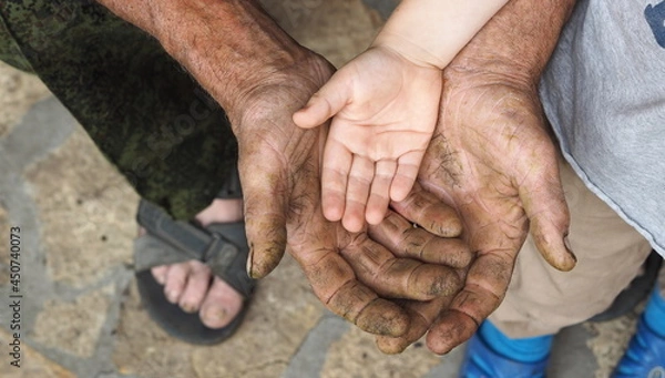 Fototapeta The hand of a child lies on the hand of a working man. Communication and continuity of two generations. Grandfather and grandson.
