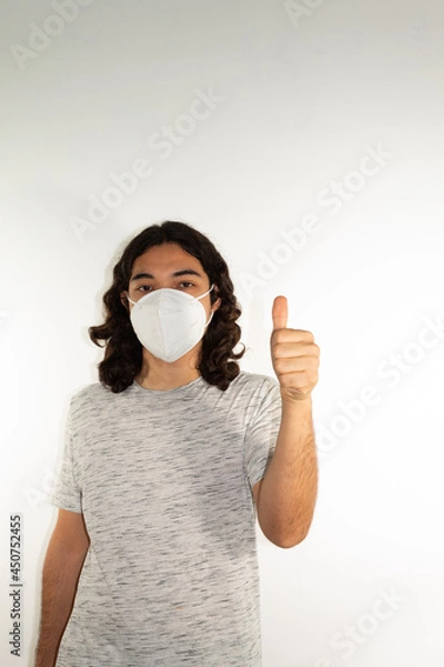 Fototapeta Hispanic man with long hair wearing a kn95 face mask on a white background with a thumb up