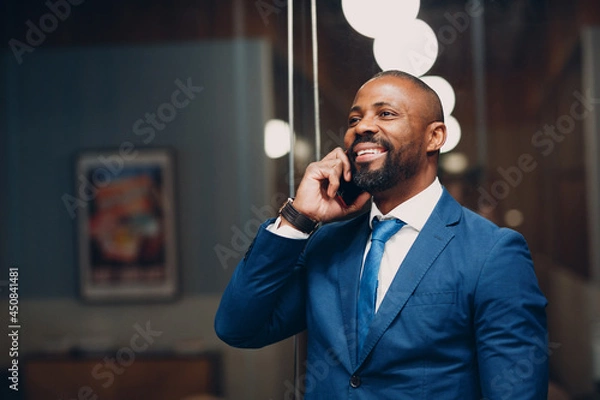Fototapeta Portrait smiling african american businessman in blue suit in office with mobile phone speaking talking smiling indoor
