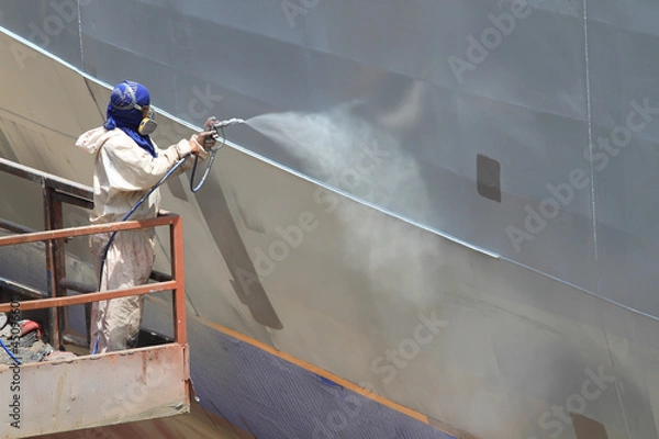Fototapeta worker painting ship hull using airbrush gray paint