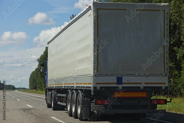 Fototapeta Beautiful van semi truck driving on the suburban highway road at Sunny summer day on blue sky with white clouds background, cargo trucking transportation logistics, back side close-up view