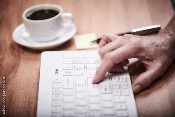 Fototapeta Woman works in the office on a wooden table. Woman's hand on keyboard. Concept workspace, working at a computer, freelance, design. Cayboard and cup of coffee. Flat lay, top view.