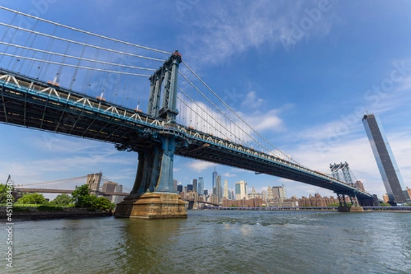 Fototapeta Manhattan Bridge crosses over the East River from the Brooklyn Bridge Park on June 20, 2021 in New York City, USA. Lower Manhattan skyscraper can be seen beyond the bridge.