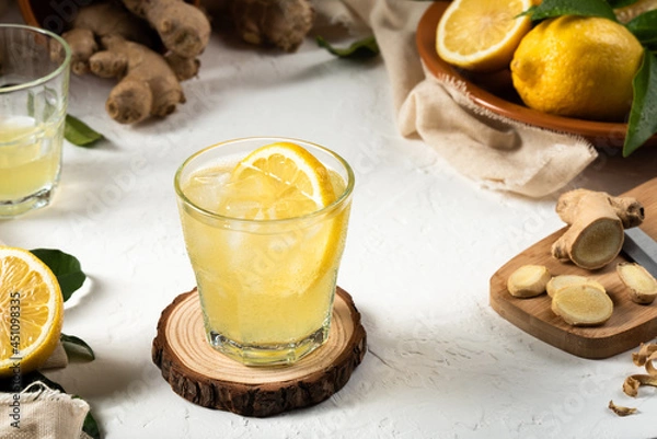 Fototapeta Detox lemon and ginger drink, with ice and a slice of lemon inside the glass, as an immune boosting and weight loss drink on a white textured surface, soft light