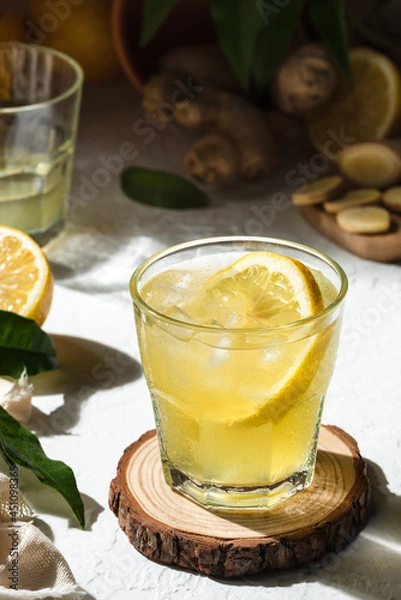 Fototapeta Fresh lemon drink with ginger and a slice of lemon inside the glass, as an immune boosting and weight loss drink, on a white surface, hard light