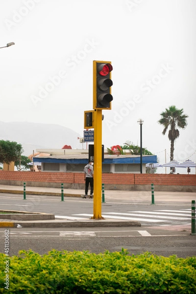 Obraz A red yellow traffic light surrounded by green areas, avenues and businesses. Traffic signs drawn on the runway and cloudy weather