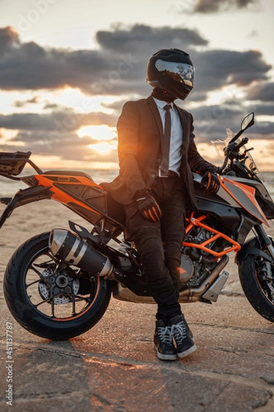Fototapeta Man dressed in suit and helmet posing on beach with bike