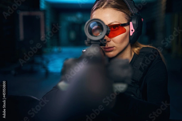 Fototapeta Serious woman using a telescopic sight mounted on the weapon