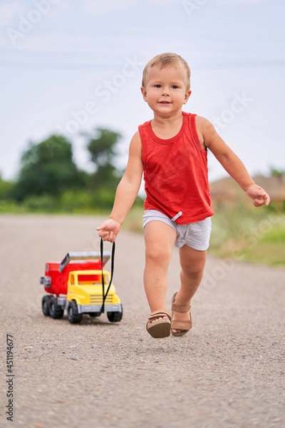 Fototapeta Cute Little Boy Plays in Outside with Toy Car. Boy Pulling Toy Car Behind Him