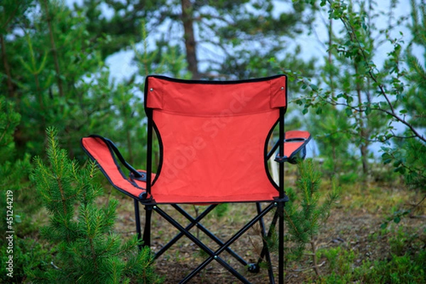 Obraz Lovely place. red tourist folder chair in the spruce forest