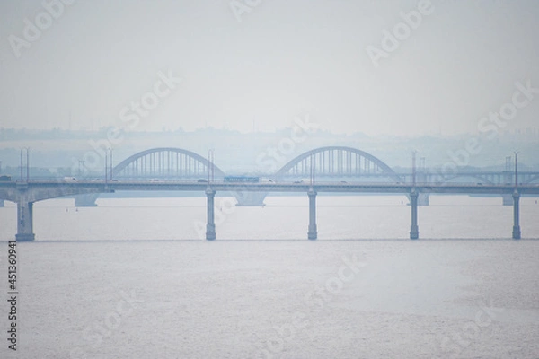 Fototapeta View of the railway and road bridges over a wide river, filmed on a cloudy, foggy day.