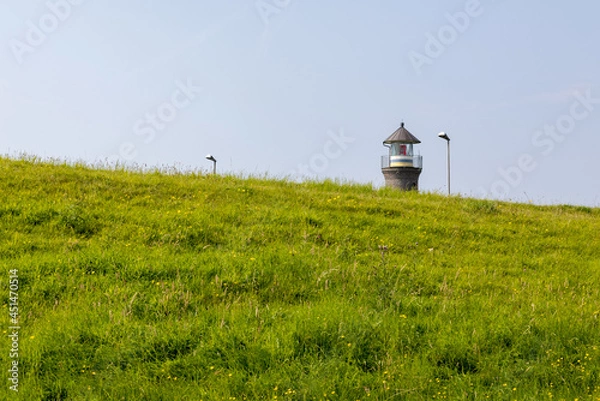 Obraz Lighthouse top behind a grass-covered dike on the North Sea 