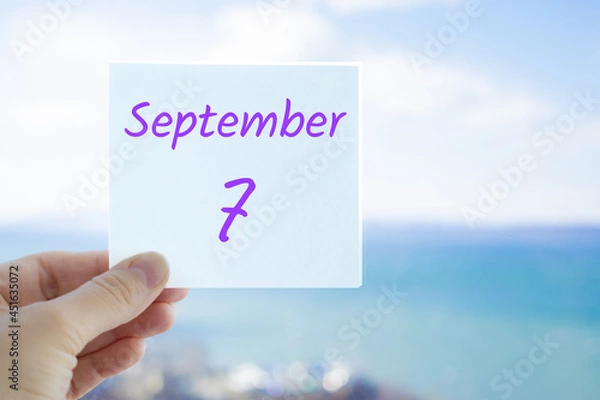 Fototapeta 7th September. Hand holding sticker with text September 7 on the blurred background of the sea and sky. Copy space for text. Month in calendar concept