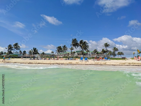 Fototapeta Cayo Coco, Cuba, May 16, 2021: Nice view of the sandy beach with turquoise water and palm trees. People are resting by the ocean.