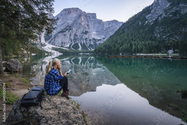 Obraz Woman reading e-book at Pragser Wildsee with reflected mountains on lake surface. Dolomites, Italy