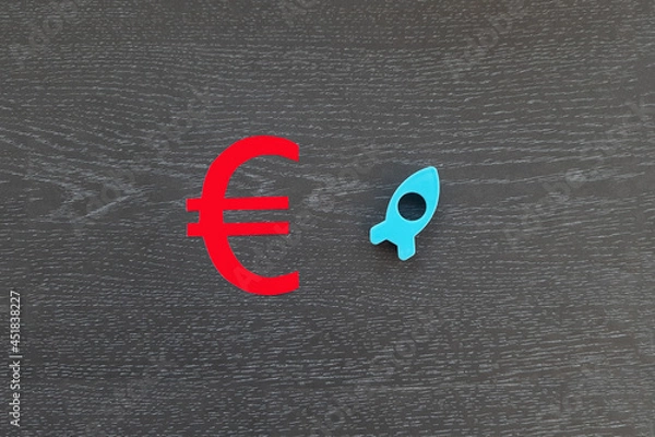 Fototapeta The euro sign is red. a rocket flying up is blue on a dark background. The concept of financial cash growth.