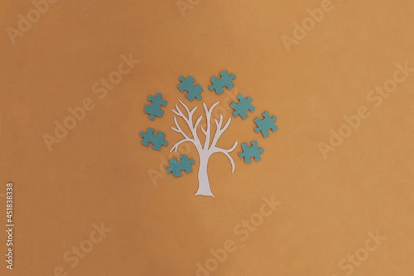 Fototapeta A tree, a crown of blue puzzles on a light brown background. Joint work, project. The result of the interaction.