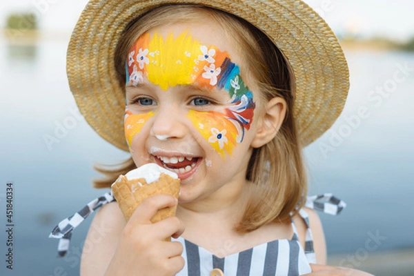 Fototapeta Happy child with face art paint eating ice-cream at summertime