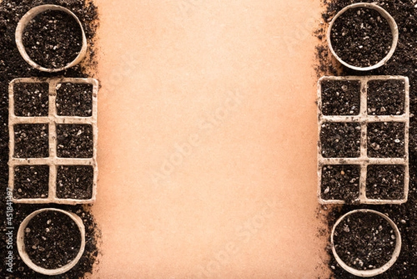 Fototapeta Biodegradable peat pots and peat trays filled with potting soil made of peat, worm humus and perlite, on a raw surface with copy space in the middle, seed starting concept.