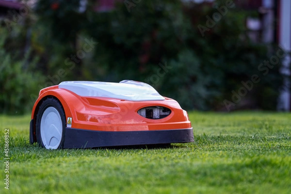 Fototapeta Automatic lawn robot mower moves on the short cut grass, lawn. Close up side view with blurry background