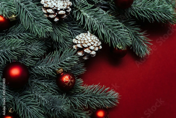 Fototapeta Space for text between Christmas tree branches with Christmas decorations and balls on a red background. Christmas composition. Happy New Year. Space for text