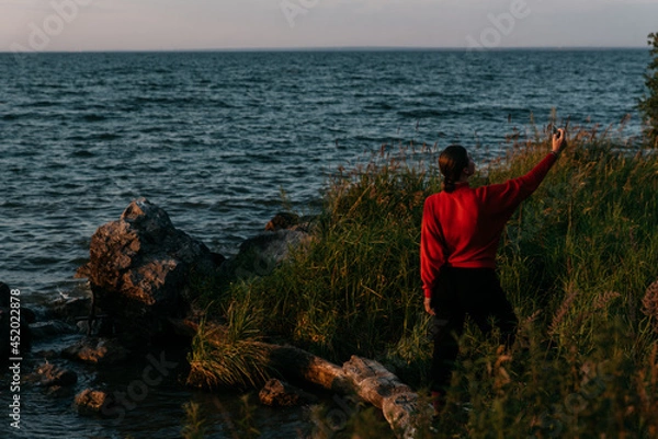 Fototapeta Photo  of a Summer Camping Activity. Travel location of popular tourist outdoor. View of beautiful Sea Landscape and Woman make selfie. Vacation by the lake in a camp with a bonfire and tent