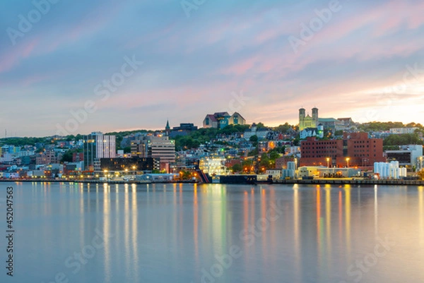 Fototapeta St. John's, Newfoundland, waterfront harbour at sunset. The lights on the water are bright yellow and orange which are reflecting from the skyline in the stillness of the smooth water.  