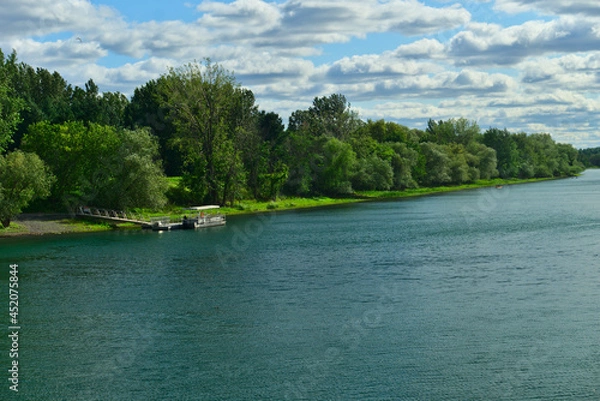 Fototapeta A boat in the river in between the islands of Boucherville national park in Lawrence (Laurent) River, Montreal, QC on a cloudy summer day. The trees and grass on the river banks