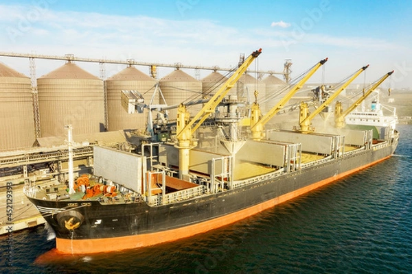 Obraz Loading grain into holds of sea cargo vessel through an automatic line in seaport from silos of grain storage. Bunkering of dry cargo ship with grain