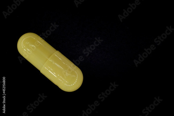 Fototapeta yellow pill in a capsule on a black, rough background, macro photo