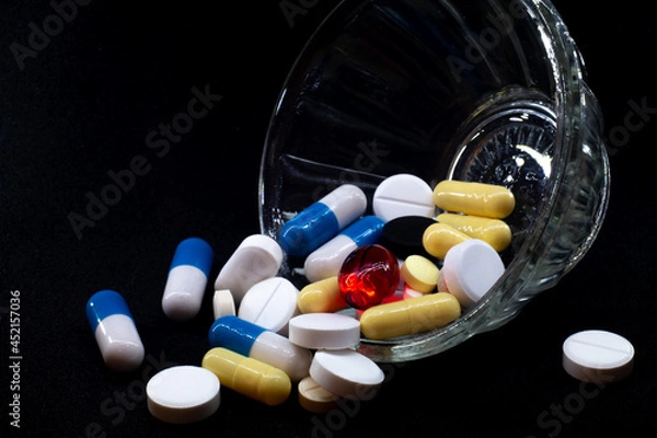 Fototapeta pills of different shapes and colors on a black background in a glass bowl. macro photo
