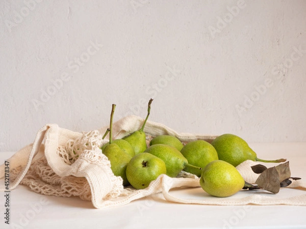 Fototapeta Ripe garden green pears in a light cotton string bag on a white background in the morning light