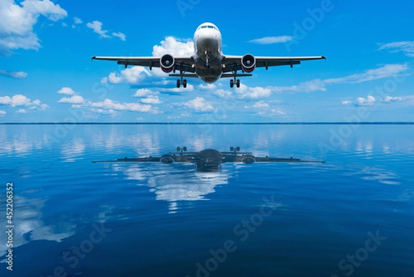 Fototapeta Flight of the plane above the calm water surface of the lake.