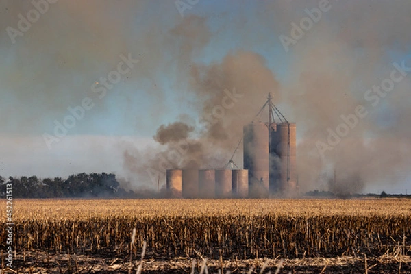 Fototapeta Wide angle landscape shot of a silo in a burning agriculture field of crops