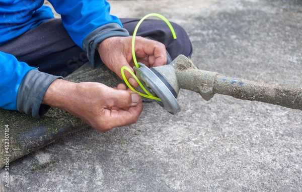 Fototapeta Gardener's hand holding a trimmer head and replacing the line in the spool in the grass trimmer