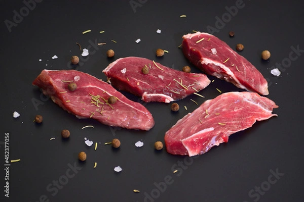 Fototapeta Slices of fresh raw beef steak with spices on black background. Top view flat lay with copy space