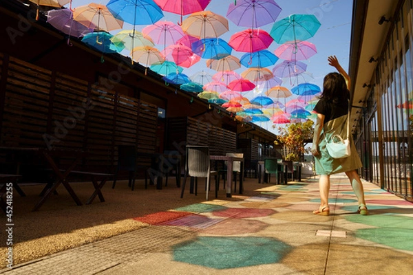 Obraz 氷見一番街のテラスで青空を彩るたくさんのビニール傘と鮮やかな傘の影に一人の女性