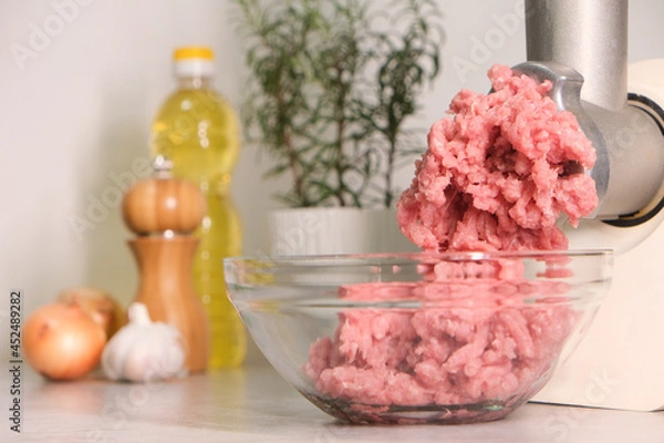 Obraz Minced meat grinder on the kitchen table in a transparent bowl.
